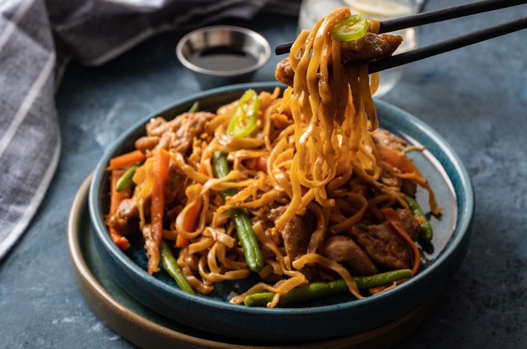 Asiatische Nudeln mit Schweinefleisch in Teriyaki-Soße, serviert mit grünen Bohnen, Möhren und Shiitake-Pilzen.